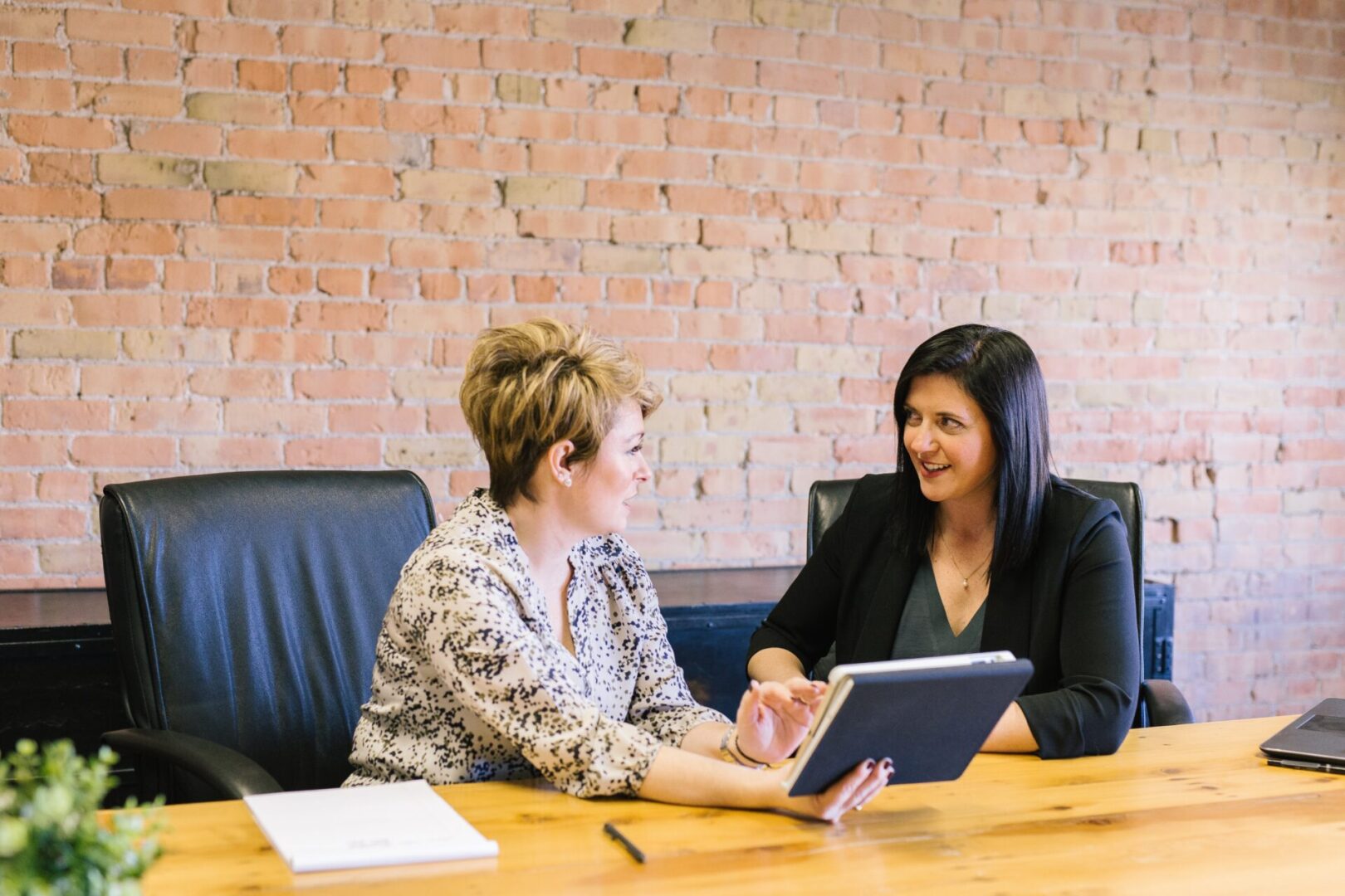 Two women sitting at a table with one of them holding an ipad.