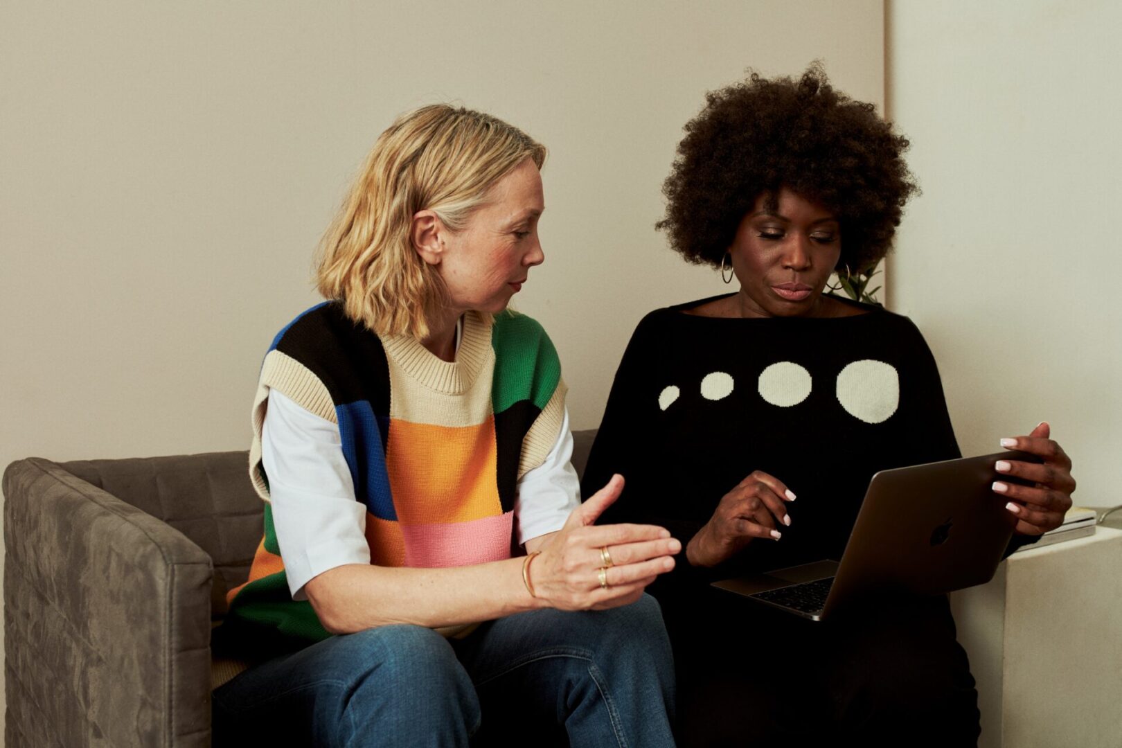 Two women sitting on a couch looking at something.