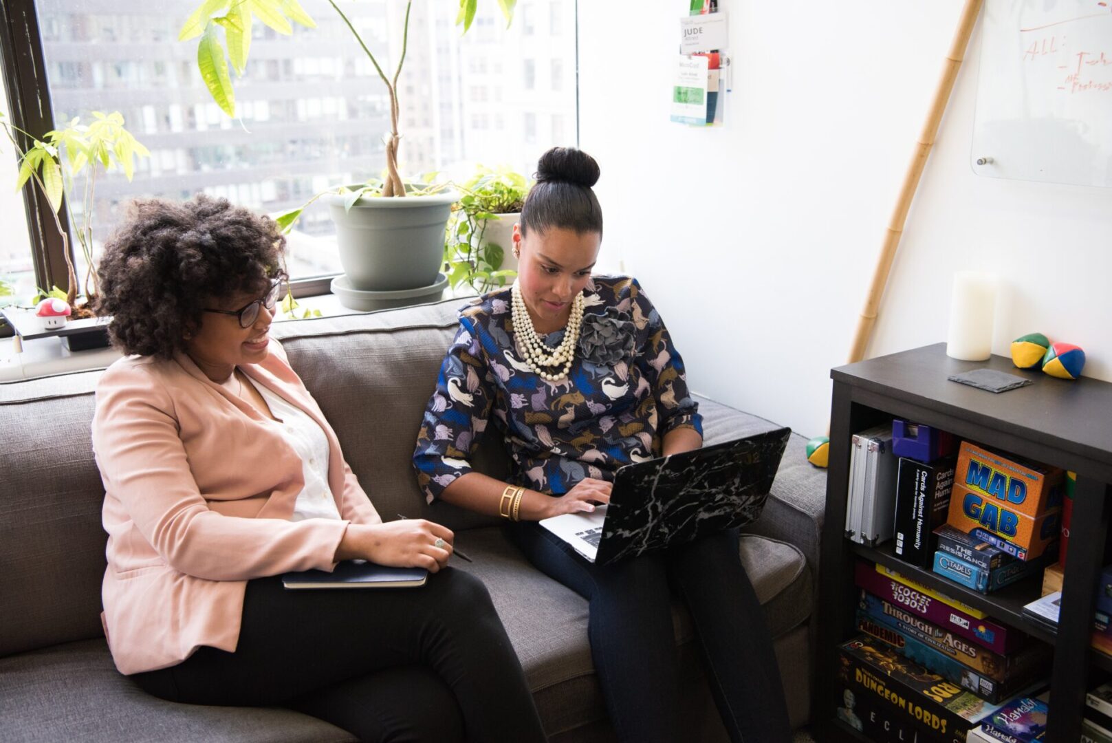 Two women sitting on a couch looking at a laptop.